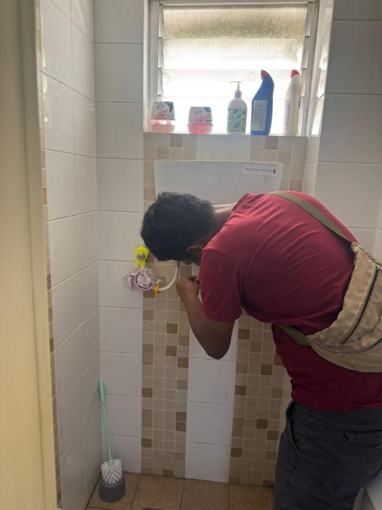 Plumber checking the inlet hose and valve of a wall-mounted toilet cistern in USJ, Subang Jaya