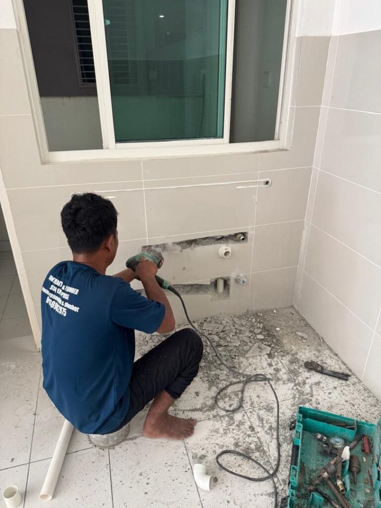 Plumber hacking bathroom wall to repair hidden leaking pipe in Petaling Jaya home